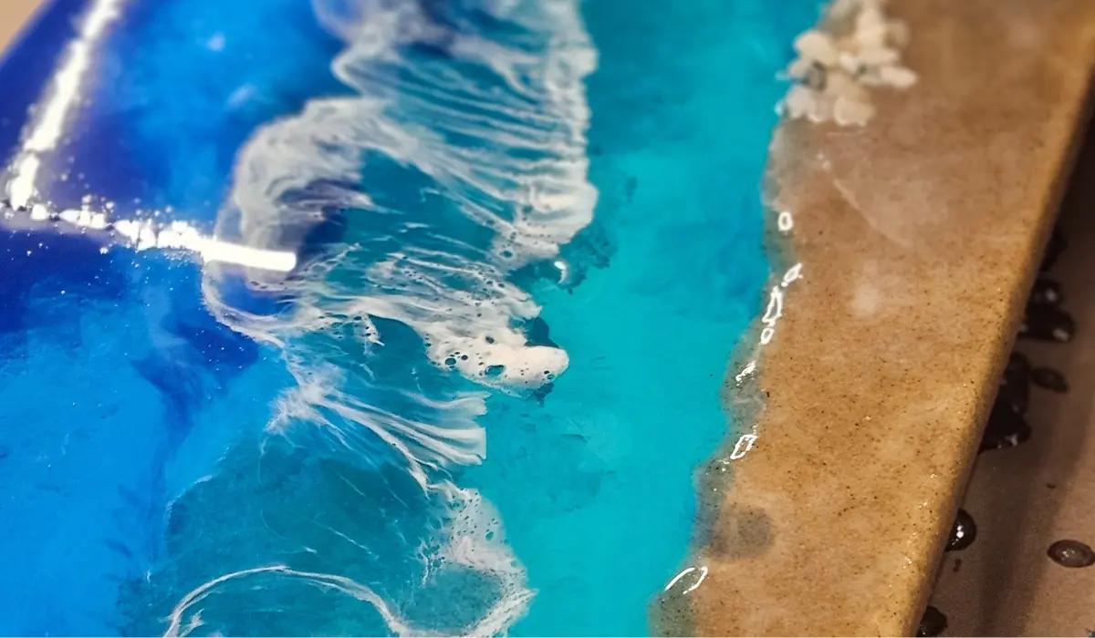 Close-up of resin beach art showing turquoise ocean waves meeting sandy shore with white foam