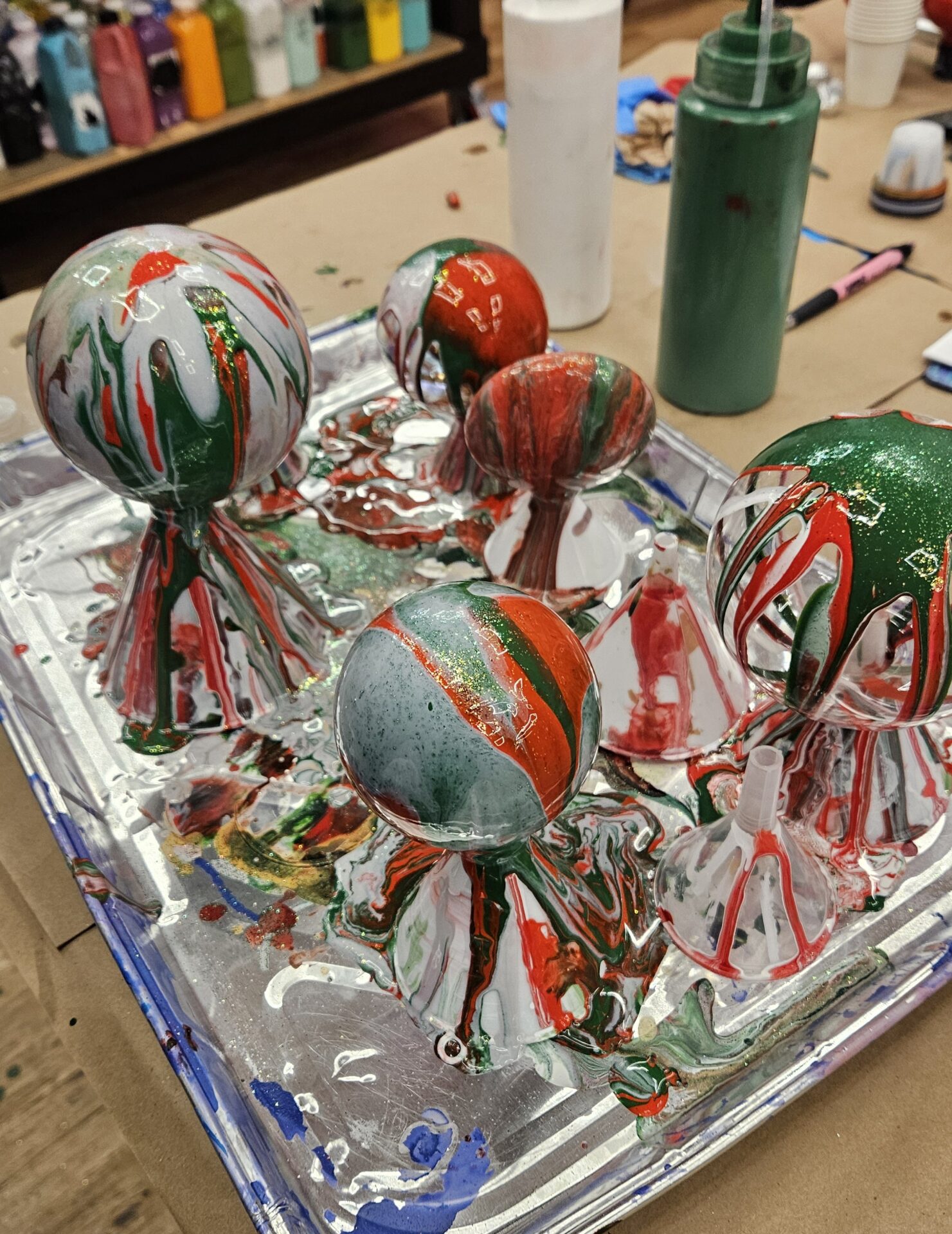 Red, green, and white marbled fluid art Christmas ornaments drying on a foil tray at Hangout for Art